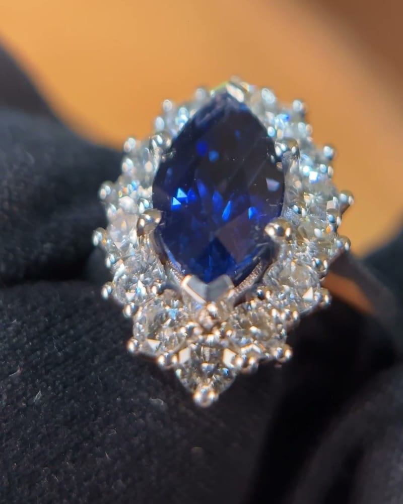 Ring with a marquise-cut blue sapphire surrounded by diamonds, held in a black glove on dark velvet
