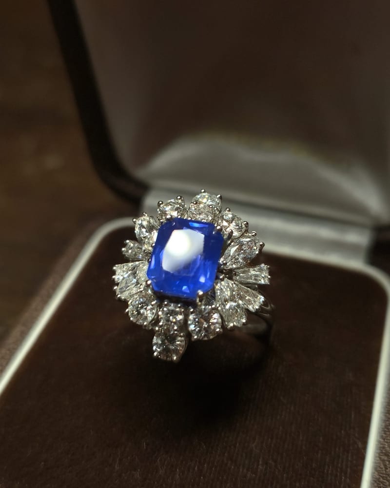 Ring with a rectangular blue sapphire surrounded by diamonds of different cuts, in its brown velvet box